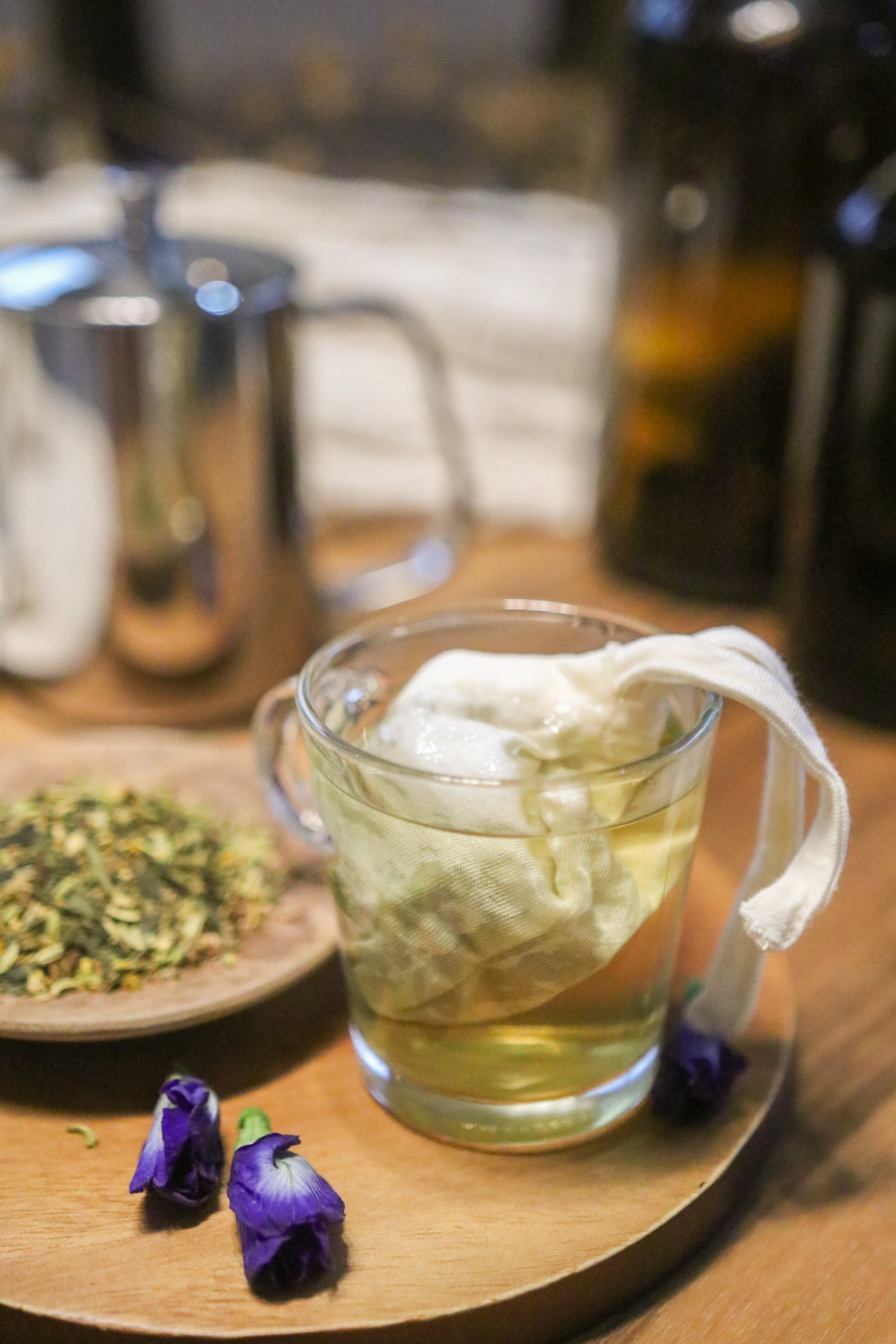 Allergy-free cotton tea bag in glass mug with herbal tea and dried flowers on wooden tray