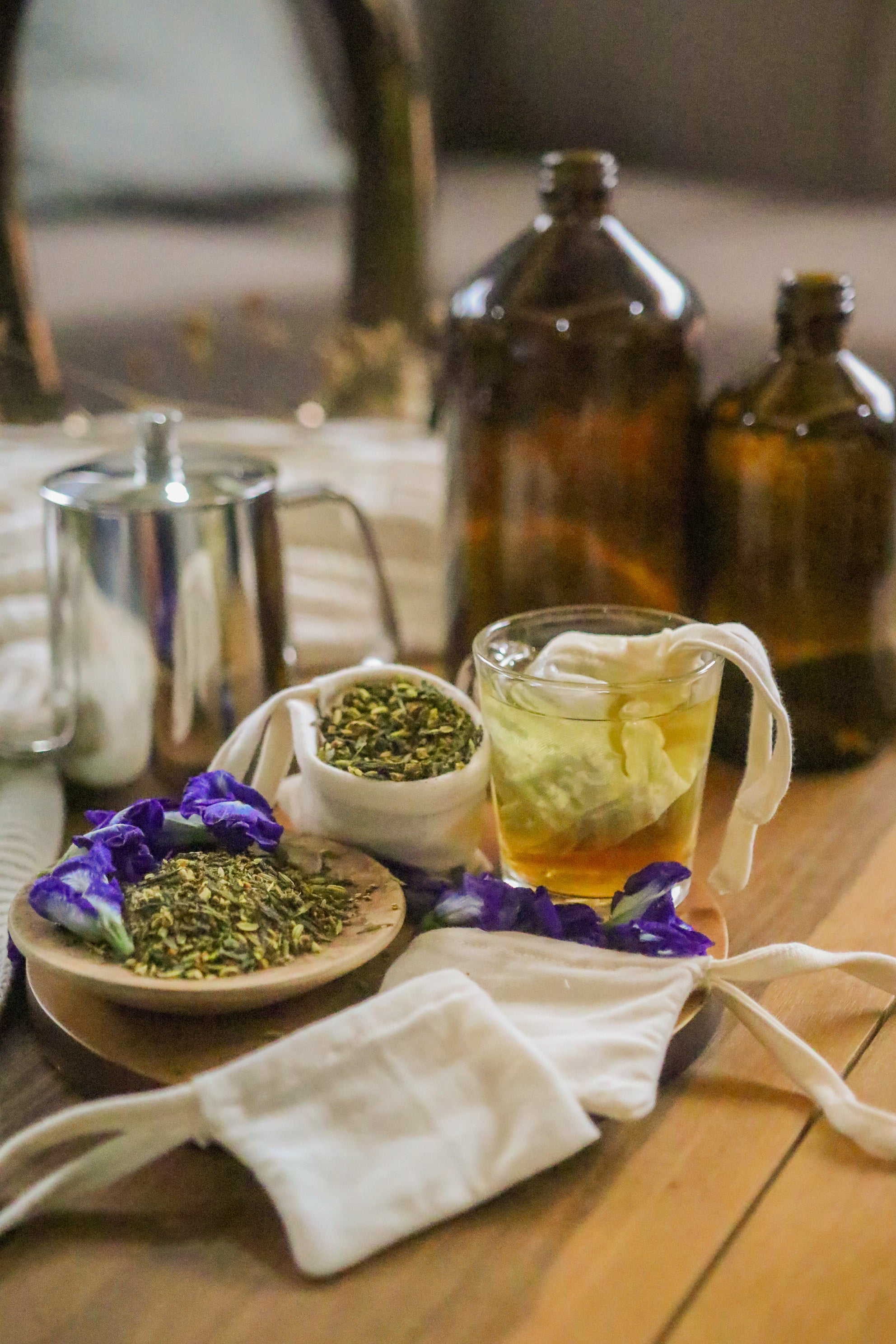 Reusable cotton tea bag with loose herbal tea, glass of tea, and fabric pouches on wooden table