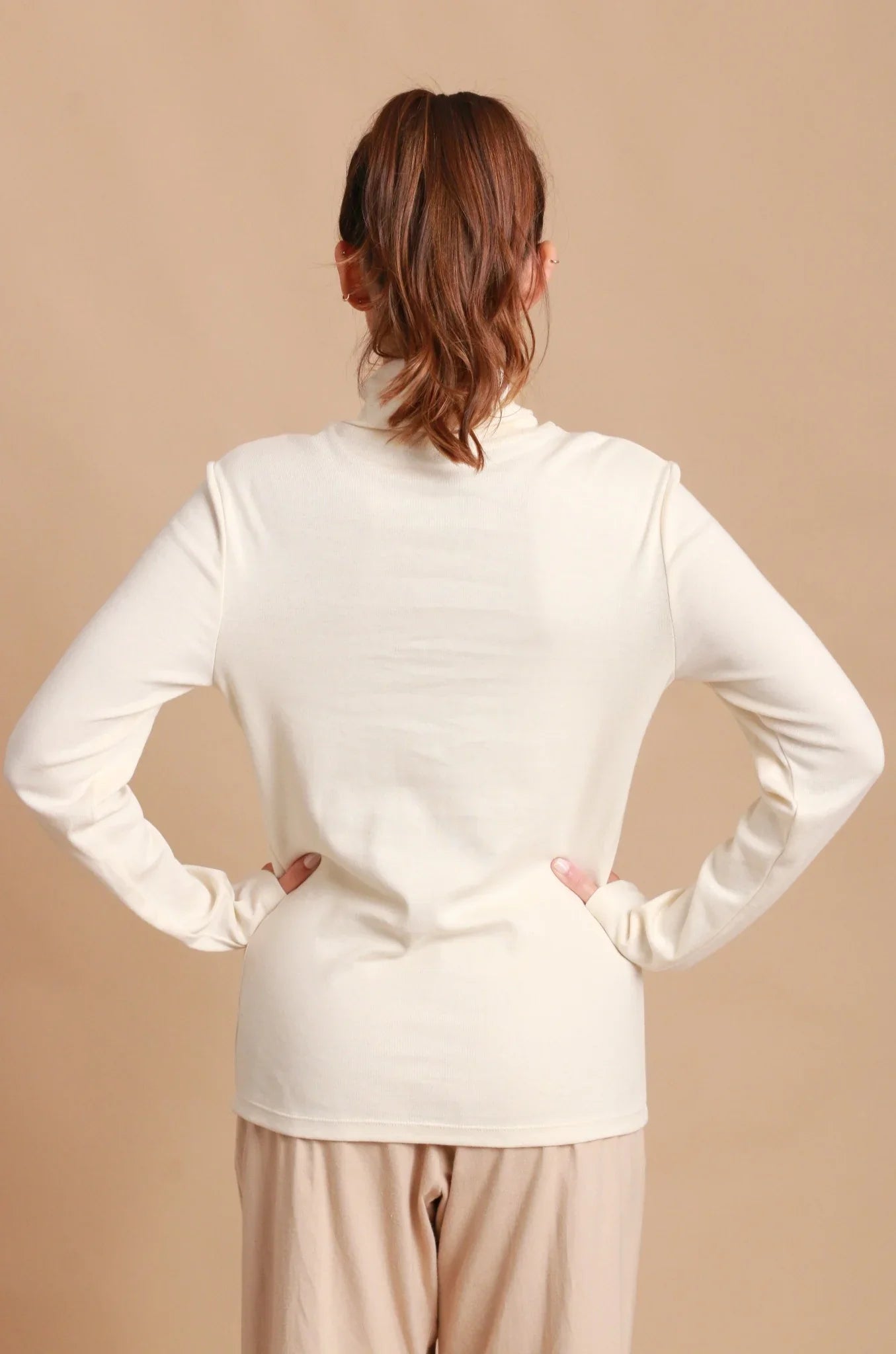 Back view of woman wearing long sleeve organic cotton cream turtleneck top