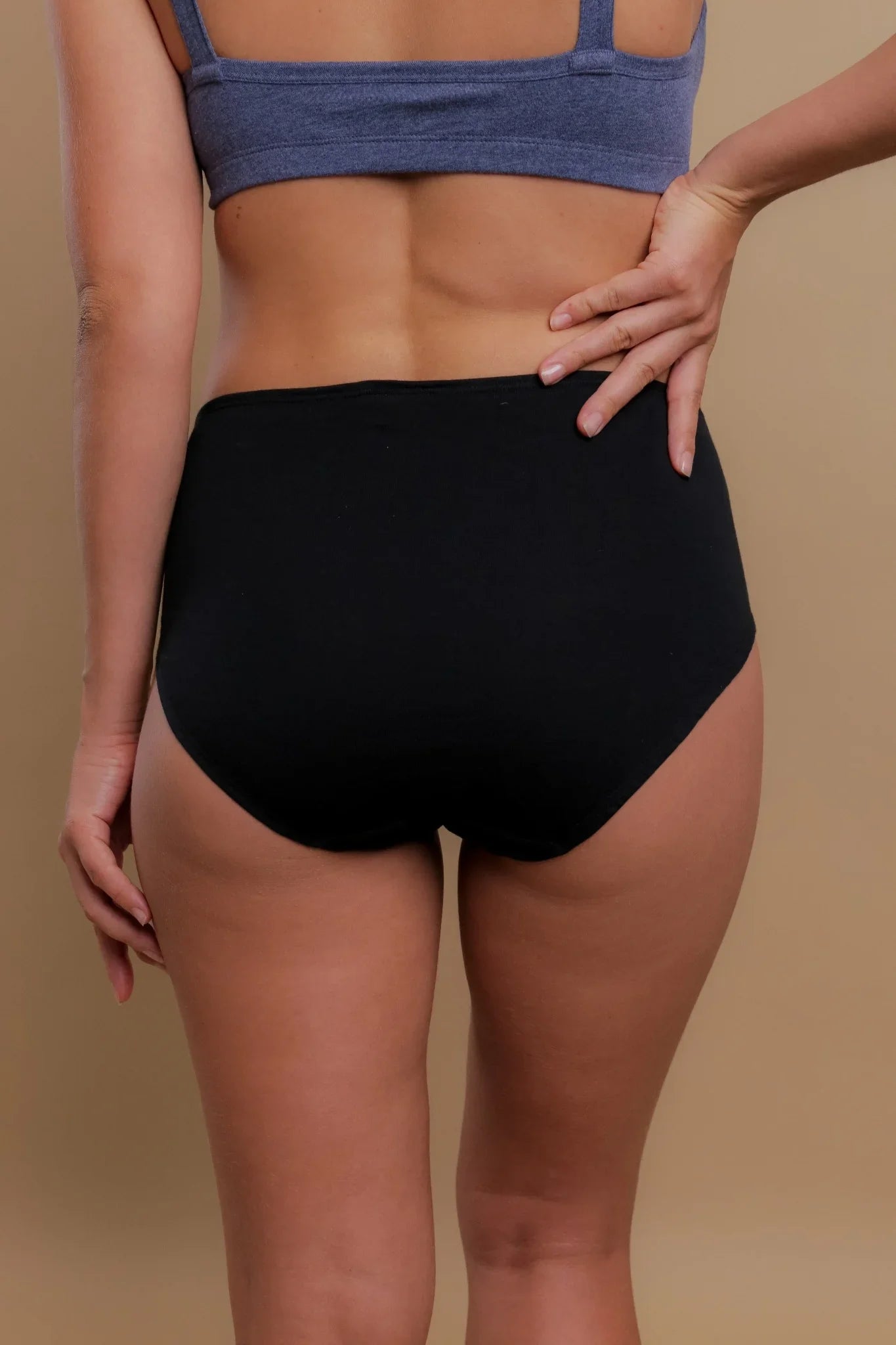 Back view of woman wearing hypoallergenic black cotton briefs and a blue bra, Cottonique apparel