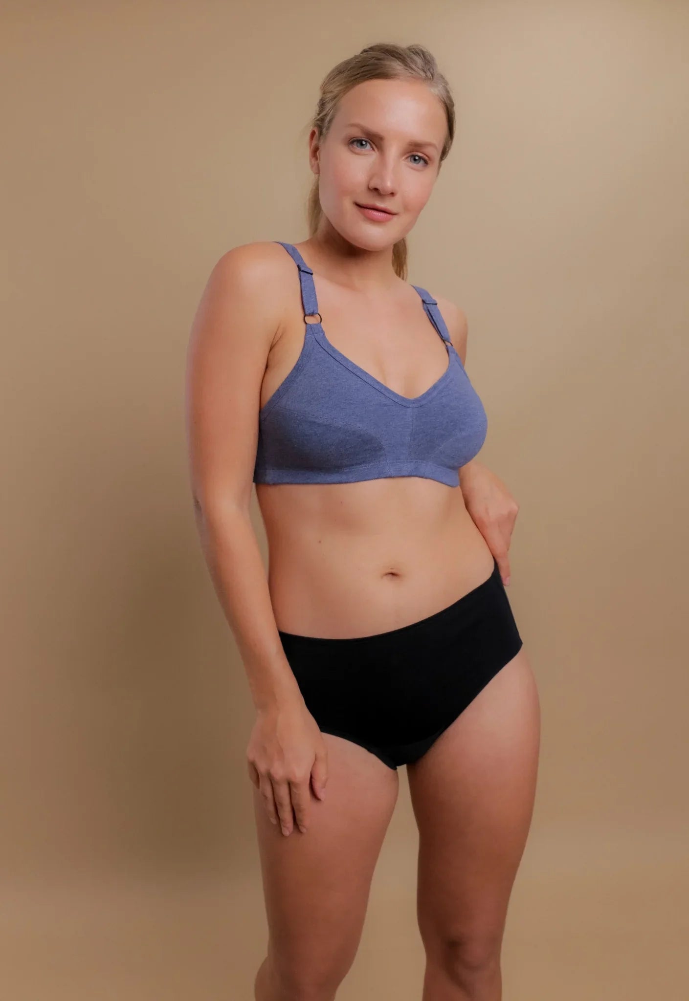 Woman modeling Cottonique allergy-free blue bra and black underwear on beige background